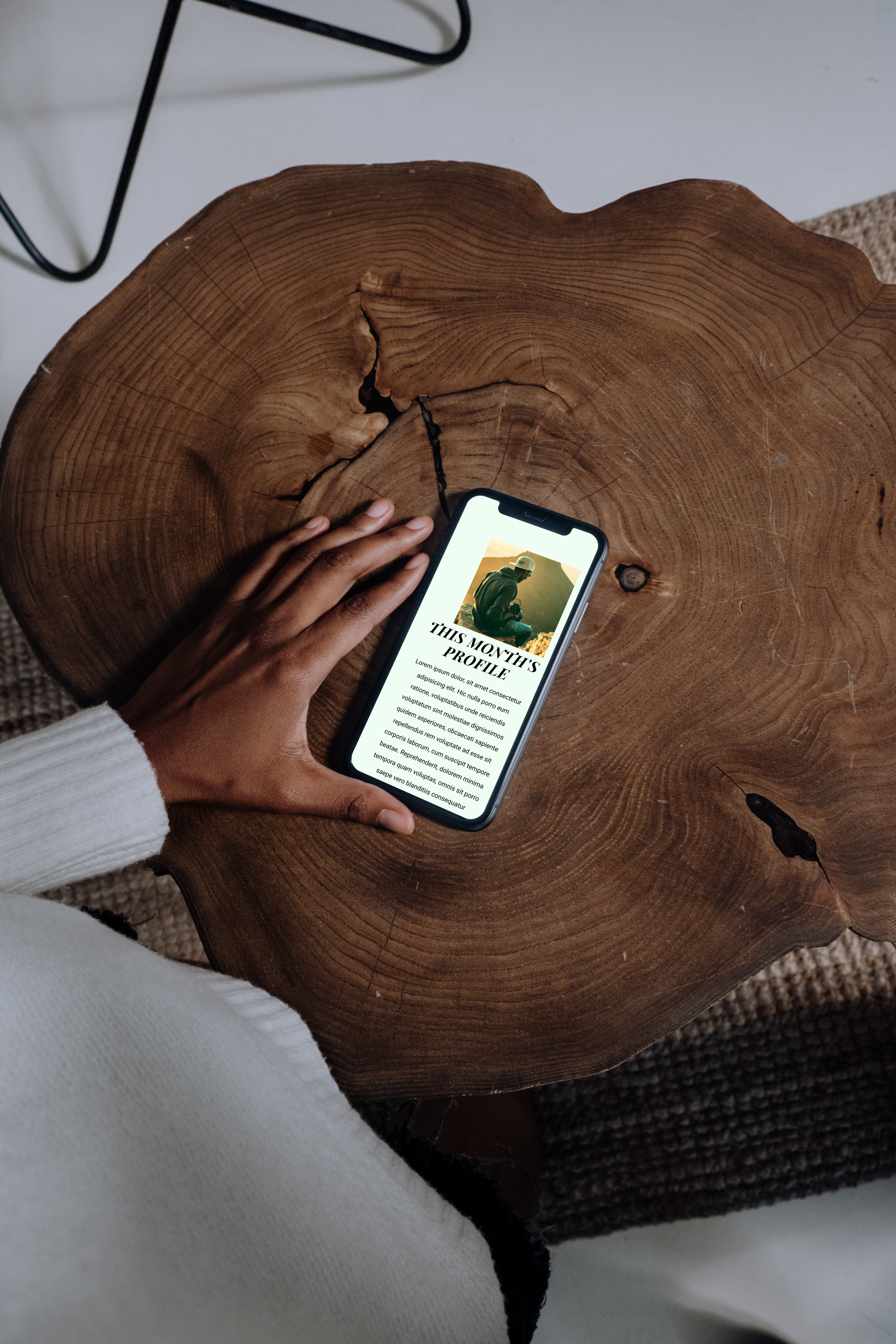 Hand resting on a wooden table scrolling a phone with image of Captured website
