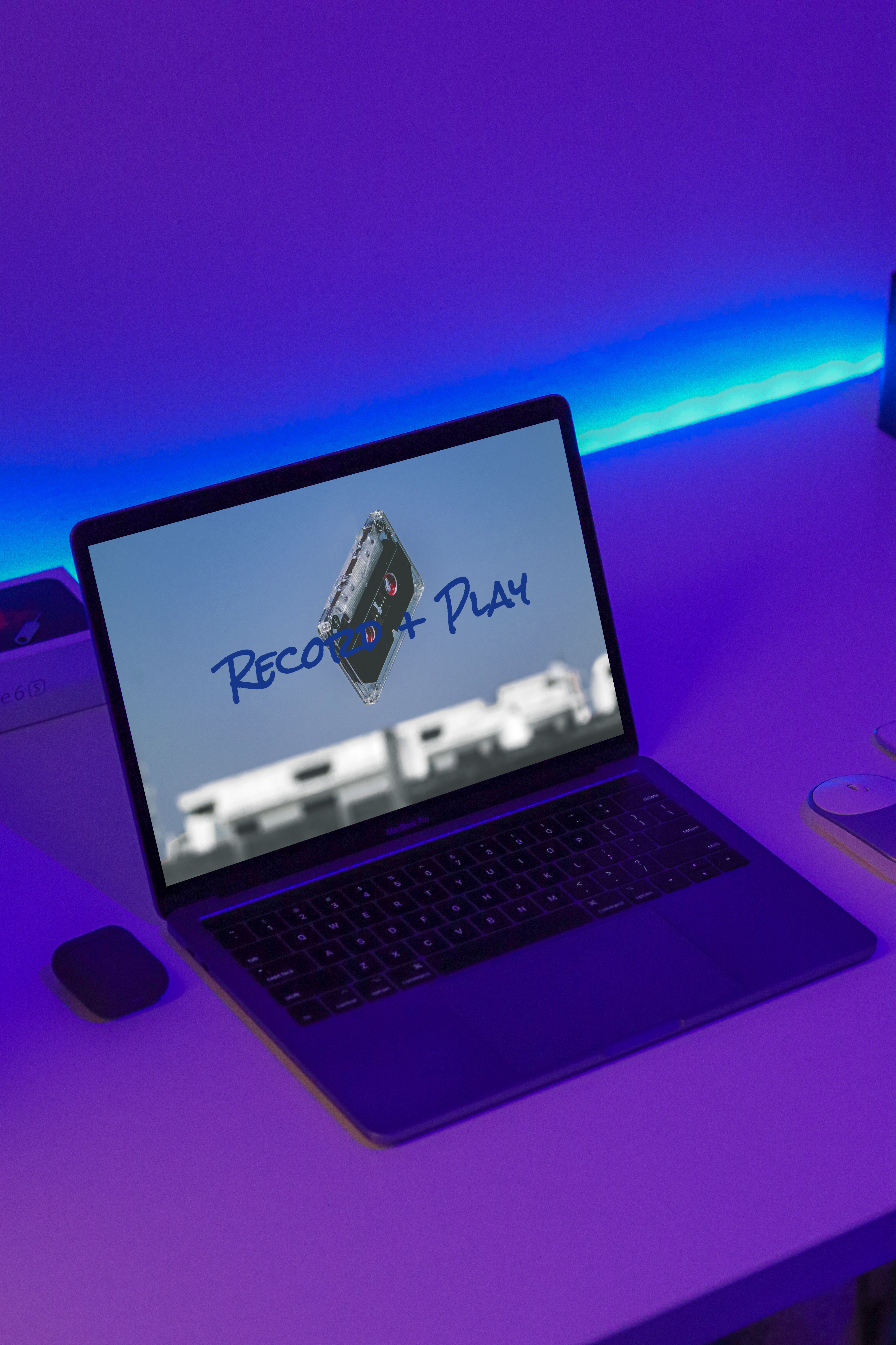 Laptop on a desk in a neon blue and pink lit room, screen displaying header of Record + Play website